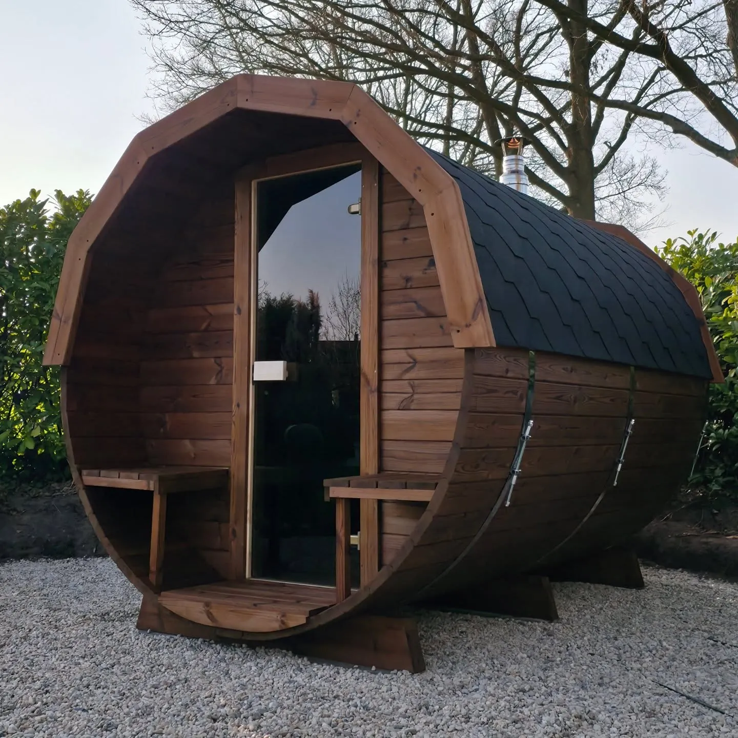 Sauna Barrel en bois foncé sur terrasse en gravier